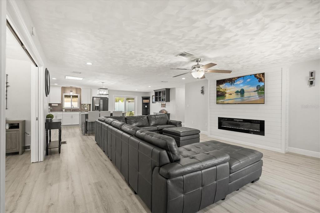 A spacious open-concept living room features a large grey sectional, fireplace, and adjacent kitchen — 1210 E CAROLINE STREET, TAVARES, FL