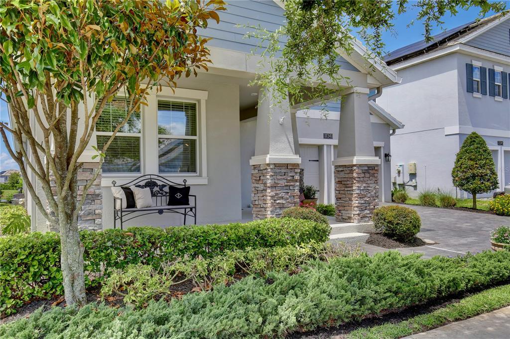 A front porch with a metal bench, stone pillars, and manicured landscaping — 11341 SATIRE STREET, ORLANDO, FL