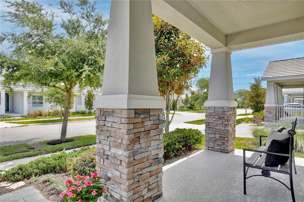 A covered front porch features stone-based columns, a concrete floor, and a metal bench — 11341 SATIRE STREET, ORLANDO, FL
