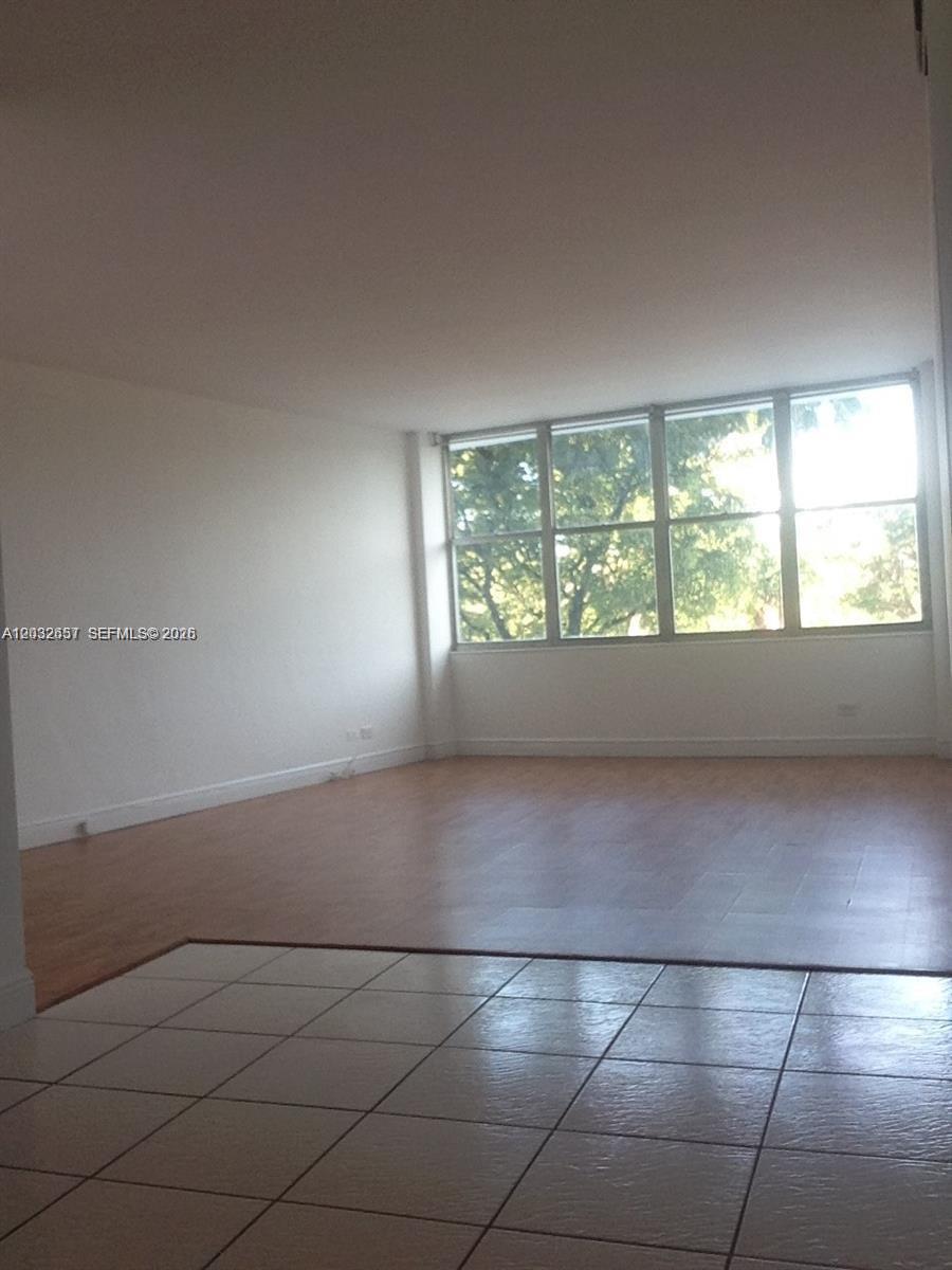 An empty room features light wood flooring and a large window wall with horizontal blinds — 7441 Wayne Ave # 2O, Miami Beach FL 33141, MIAMI BEACH, FL
