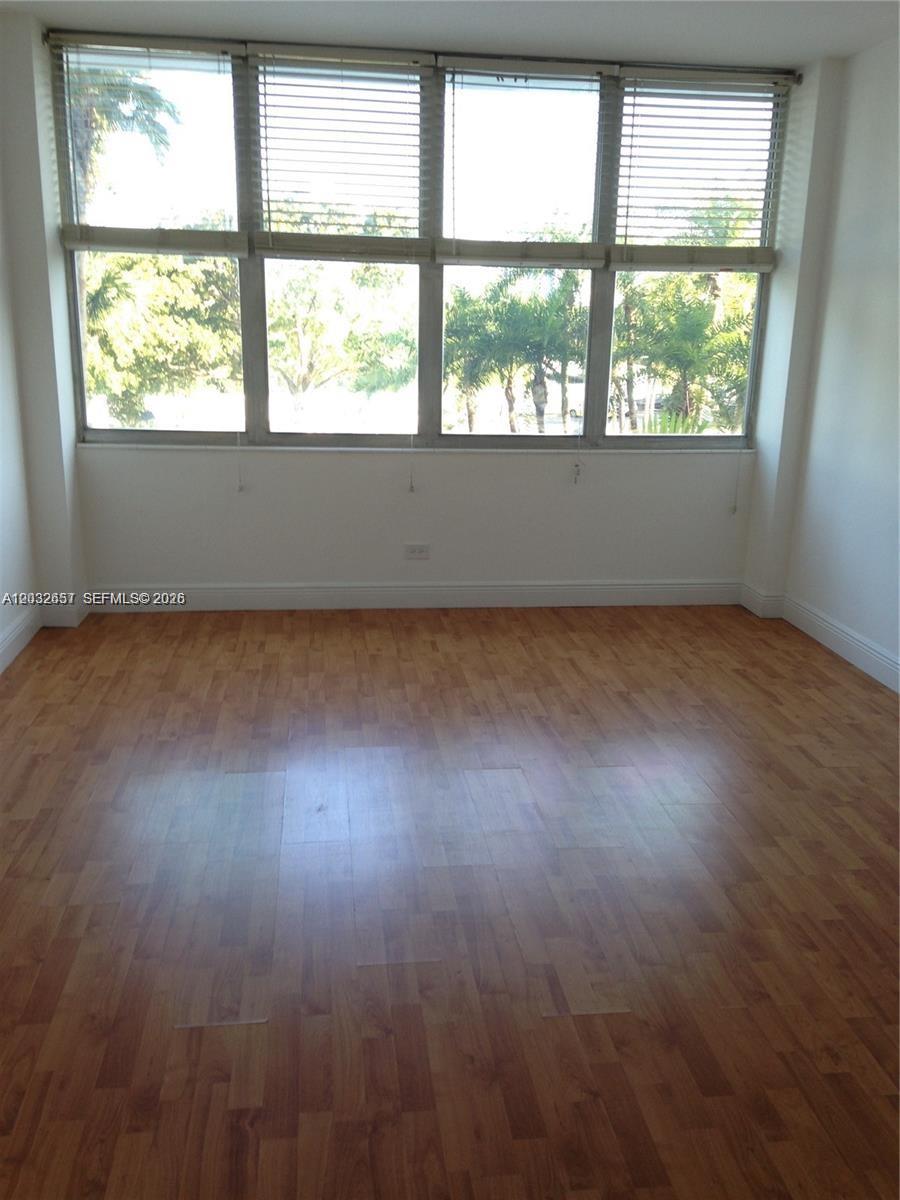 An empty room features light wood flooring, white walls, and large windows overlooking a pool — 7441 Wayne Ave # 2O, Miami Beach FL 33141, MIAMI BEACH, FL
