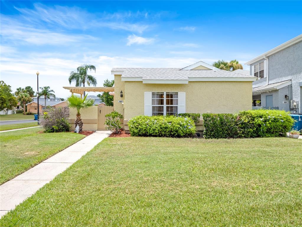 A single-story yellow stucco house features a front lawn, a walkway, and a wooden gate — 1445 MALIBU CIRCLE NE UNIT 107, PALM BAY, FL