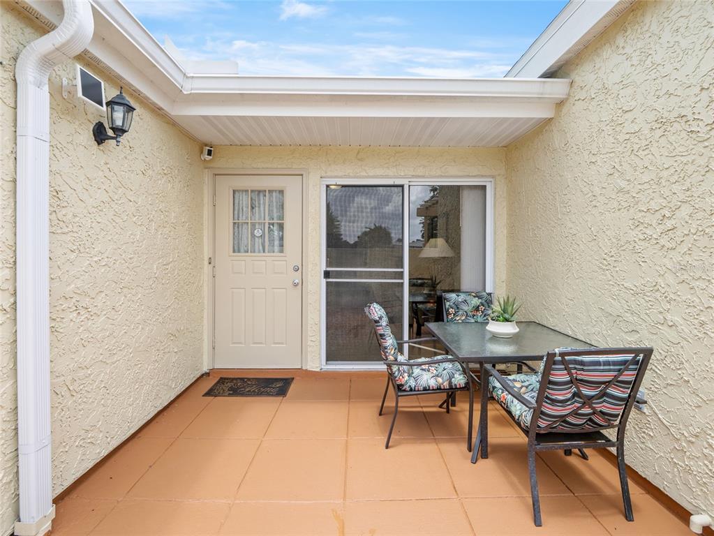 A small outdoor patio with a table, two chairs, a door, and a sliding glass door — 1445 MALIBU CIRCLE NE UNIT 107, PALM BAY, FL