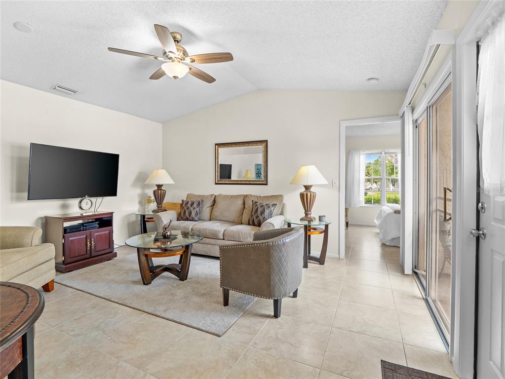 A living room features a beige sofa, a glass coffee table, and a ceiling fan — 1445 MALIBU CIRCLE NE UNIT 107, PALM BAY, FL