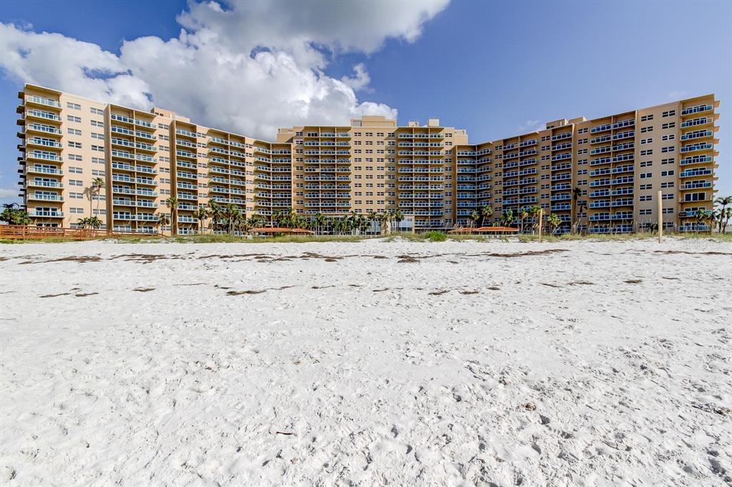 A large, multi-story tan apartment building stands behind a wide, sandy beach — 880 MANDALAY AVENUE UNIT 604, CLEARWATER BEACH, FL