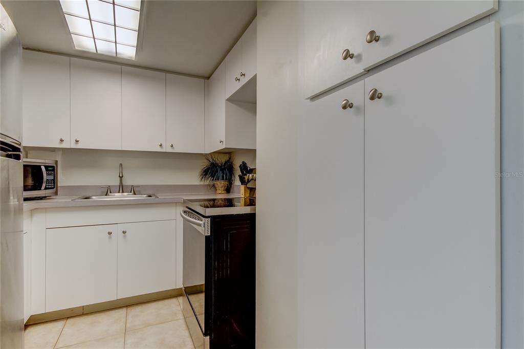 A galley kitchen features white cabinets, light countertops, a black stove, and tile flooring — 880 MANDALAY AVENUE UNIT 604, CLEARWATER BEACH, FL