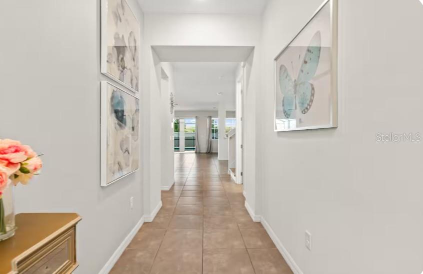 A hallway with tile flooring leads toward an open living area with large windows — 1632 NASSAU POINT TRAIL, KISSIMMEE, FL