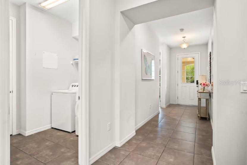 A hallway with tile flooring leads to a white front door and a laundry area — 1632 NASSAU POINT TRAIL, KISSIMMEE, FL