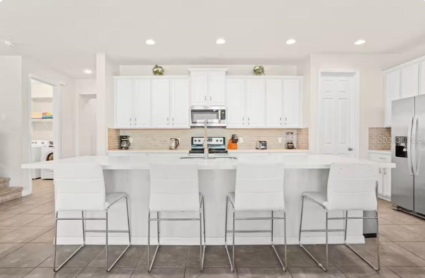 A modern kitchen features white cabinetry, a large central island with seating, and stainless appliances — 1632 NASSAU POINT TRAIL, KISSIMMEE, FL