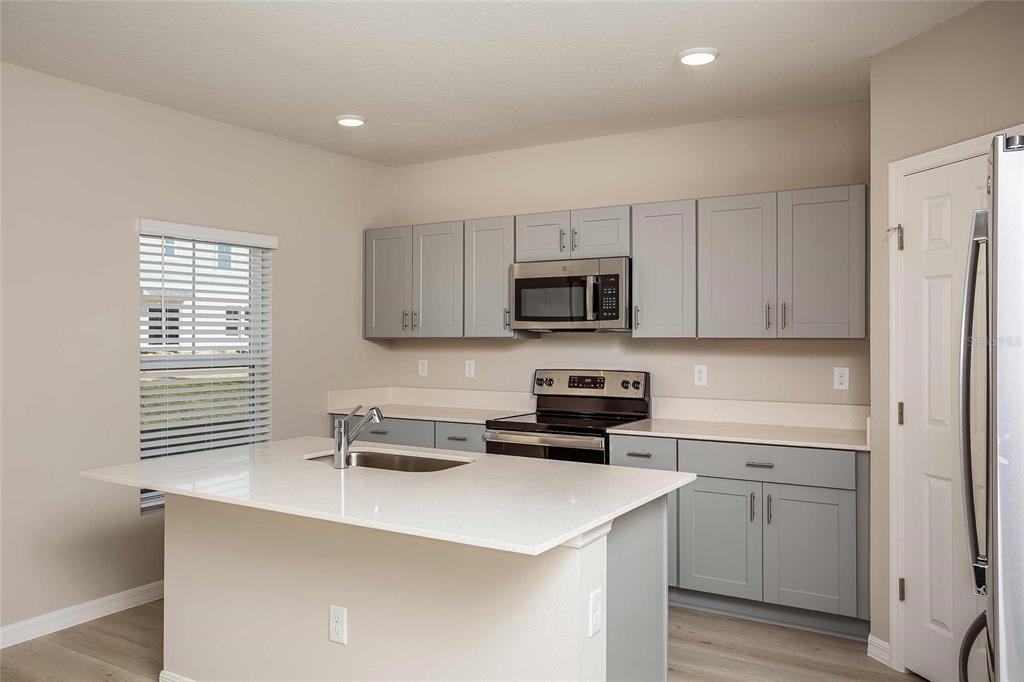 A kitchen features light gray cabinets, white countertops, a center island, and stainless steel appliances — 1807 POPPY DRIVE, LAKE HAMILTON, FL