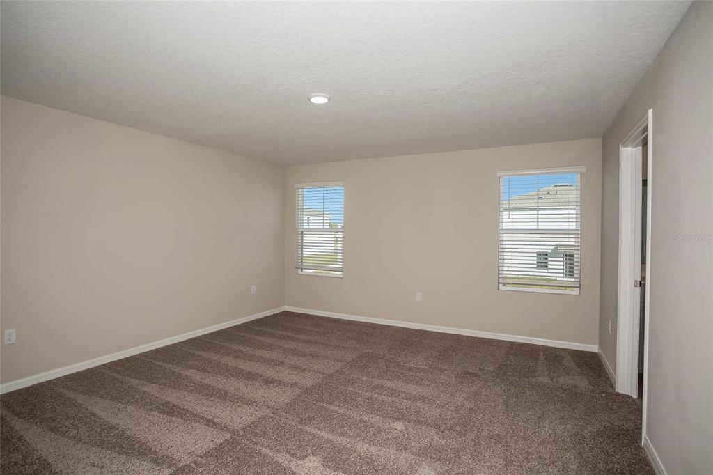 An empty bedroom features beige walls, brown carpet, two windows with blinds, and recessed lighting — 1807 POPPY DRIVE, LAKE HAMILTON, FL