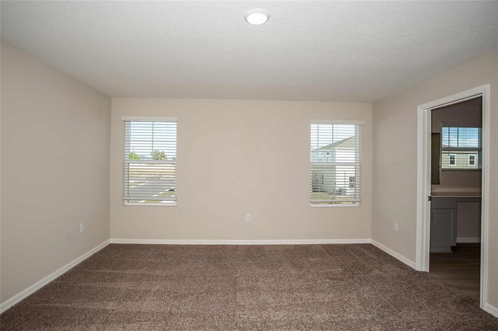 An empty bedroom features beige walls, brown carpeting, two windows with blinds, and a doorway — 1807 POPPY DRIVE, LAKE HAMILTON, FL