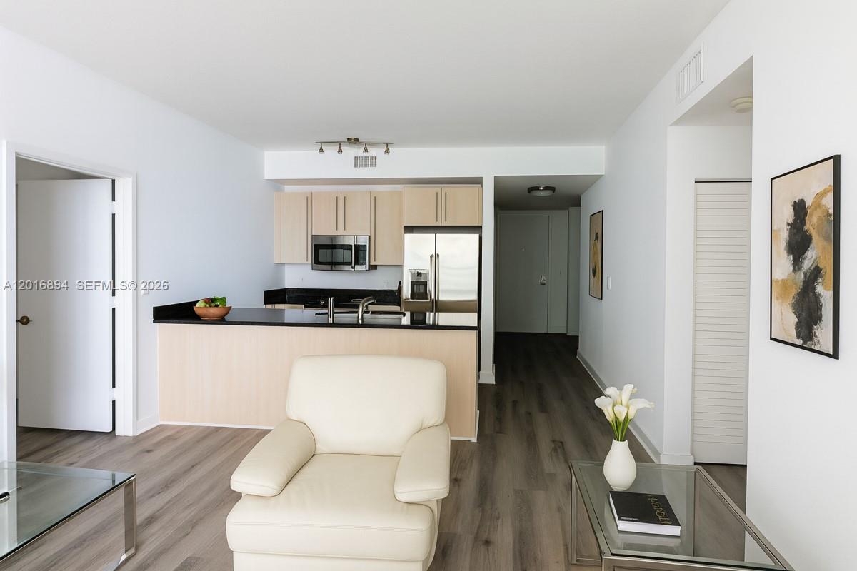 A living room with a cream armchair faces an open kitchen featuring light wood cabinets — 79 SW 12th St, Miami FL 33130, MIAMI, FL