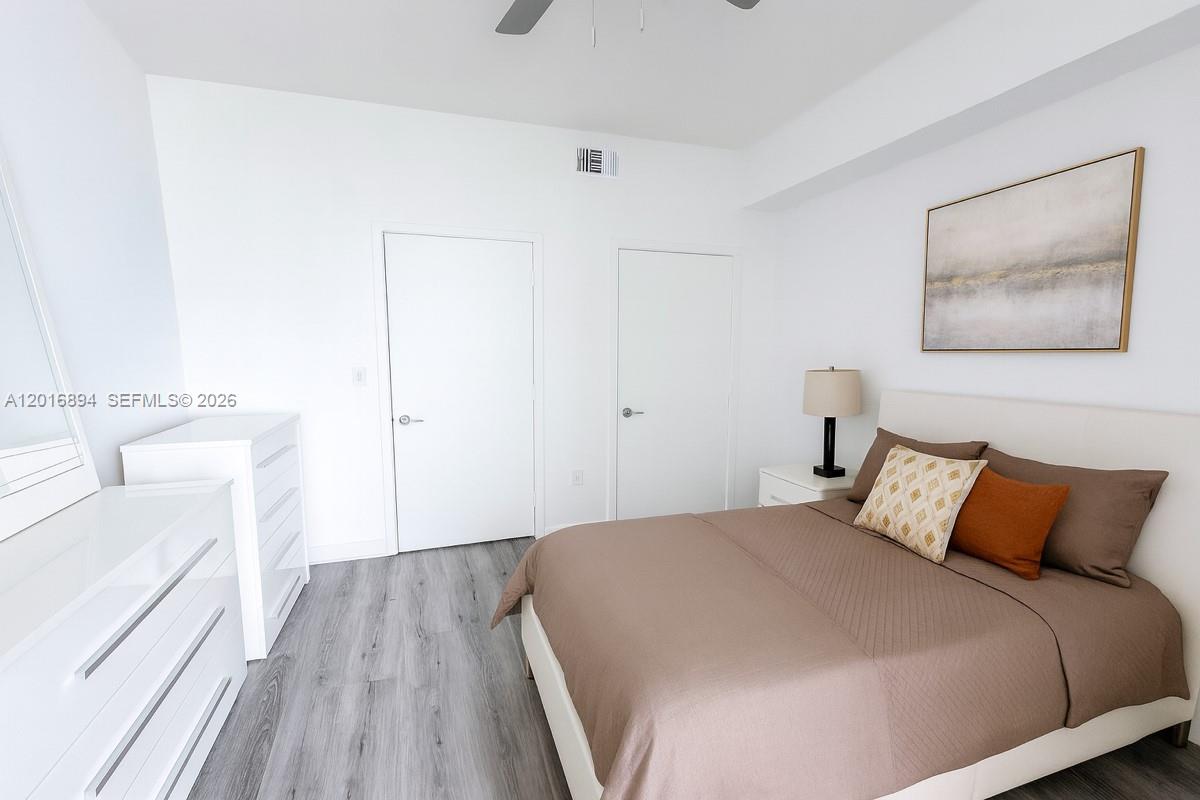 A bedroom features a bed with brown bedding, a white dresser, and light wood flooring — 79 SW 12th St, Miami FL 33130, MIAMI, FL