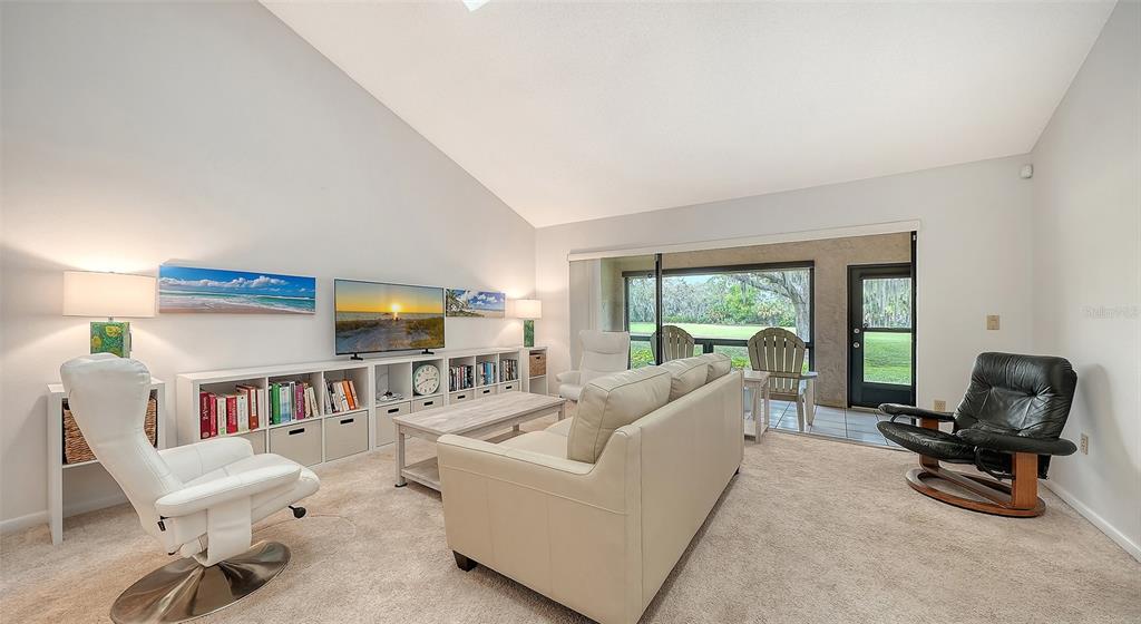 A living room with a vaulted ceiling, white sofa, two armchairs, and a sliding glass door — 4557 KINGSMERE UNIT 23, SARASOTA, FL