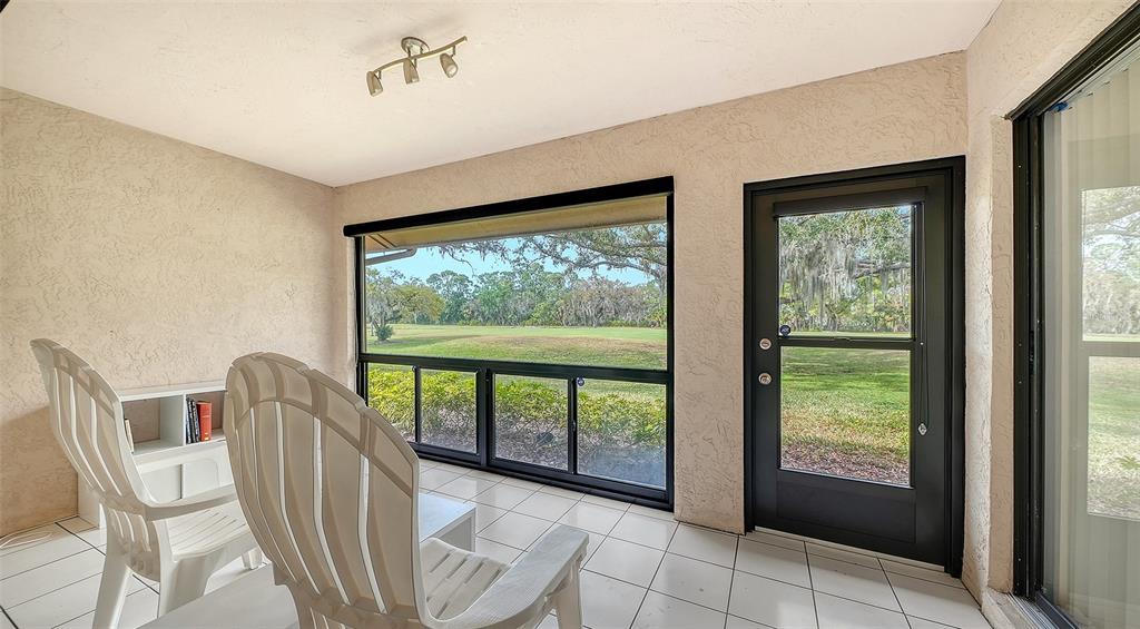 A sunroom with white tile floors, two white chairs, and a view of a golf course — 4557 KINGSMERE UNIT 23, SARASOTA, FL