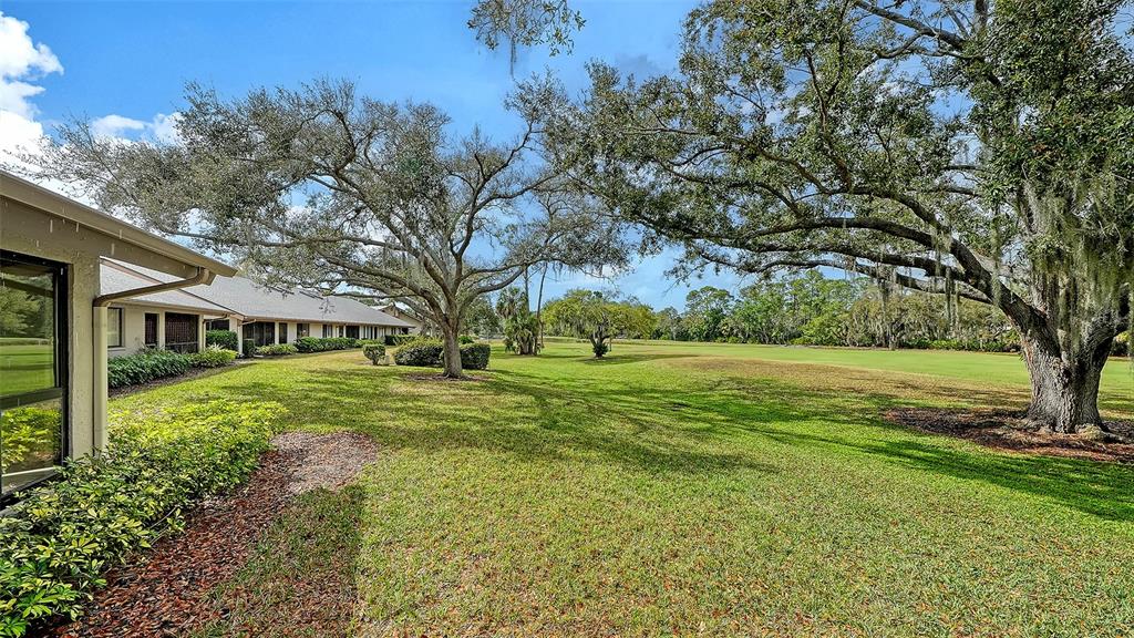 A view of a grassy lawn with large trees next to a residential building — 4557 KINGSMERE UNIT 23, SARASOTA, FL