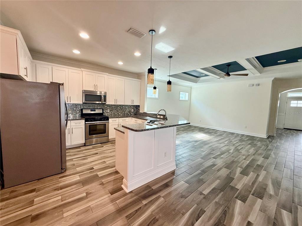 A kitchen with white cabinets, granite countertops, and wood-look tile flooring opens to a living area — 3635 NW 26TH STREET, GAINESVILLE, FL