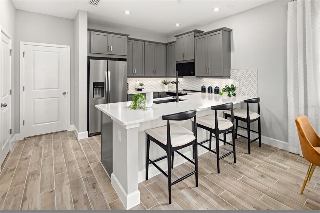 A modern kitchen features gray cabinets, a white quartz island with bar stools, and wood-look flooring — 192 RAINWOOD STREET, GROVELAND, FL
