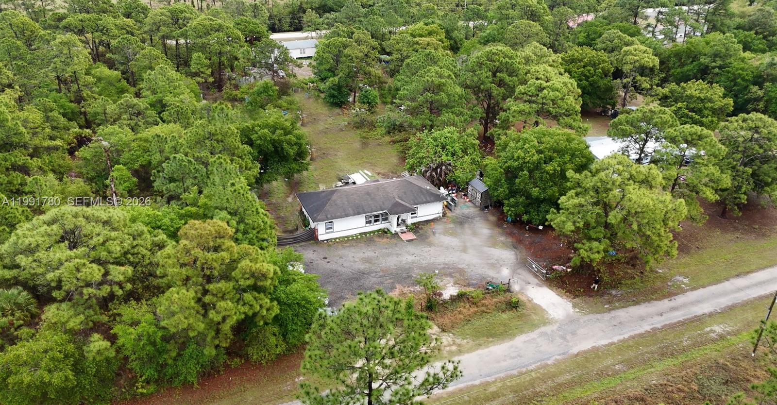 An aerial view shows a single-story white house surrounded by dense trees and gravel — 825 N Willow ST, Clewiston FL 33440, CLEWISTON, FL