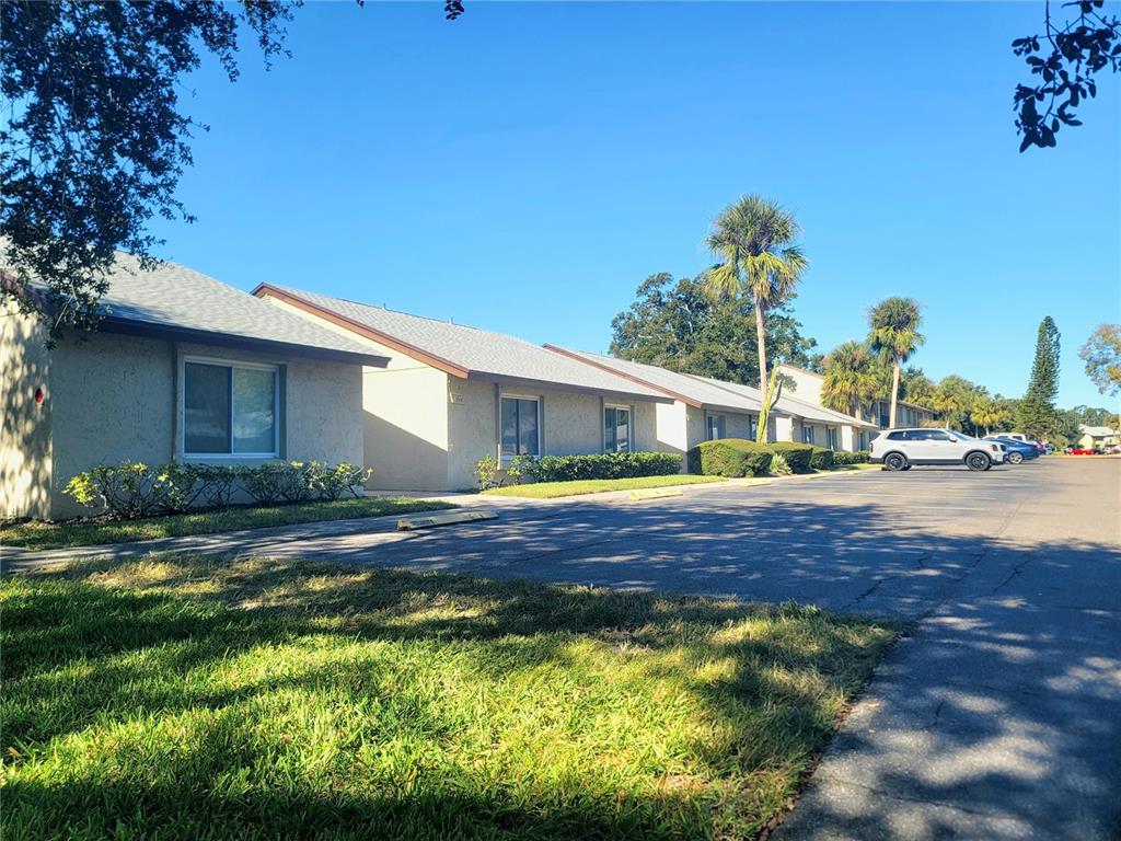 A single-story apartment building with a parking lot and palm trees under a clear sky — 4215 EAST BAY DRIVE UNIT 1508B, CLEARWATER, FL