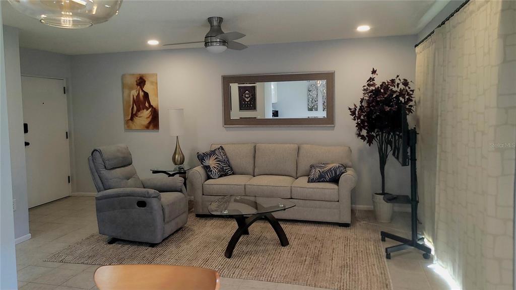 A living room features a light gray sofa, a matching recliner, and a glass coffee table — 4215 EAST BAY DRIVE UNIT 1508B, CLEARWATER, FL