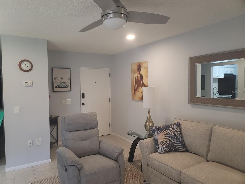 A living room features a gray recliner, a sofa, a ceiling fan, and wall art — 4215 EAST BAY DRIVE UNIT 1508B, CLEARWATER, FL