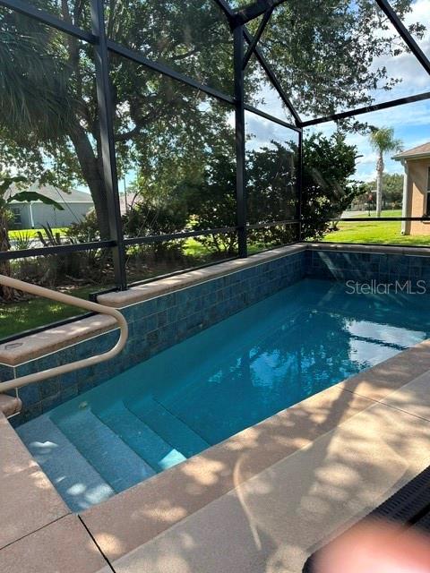 A small rectangular swimming pool with blue tile trim is enclosed by a screened lanai — 992 RIDGELAND PATH, THE VILLAGES, FL