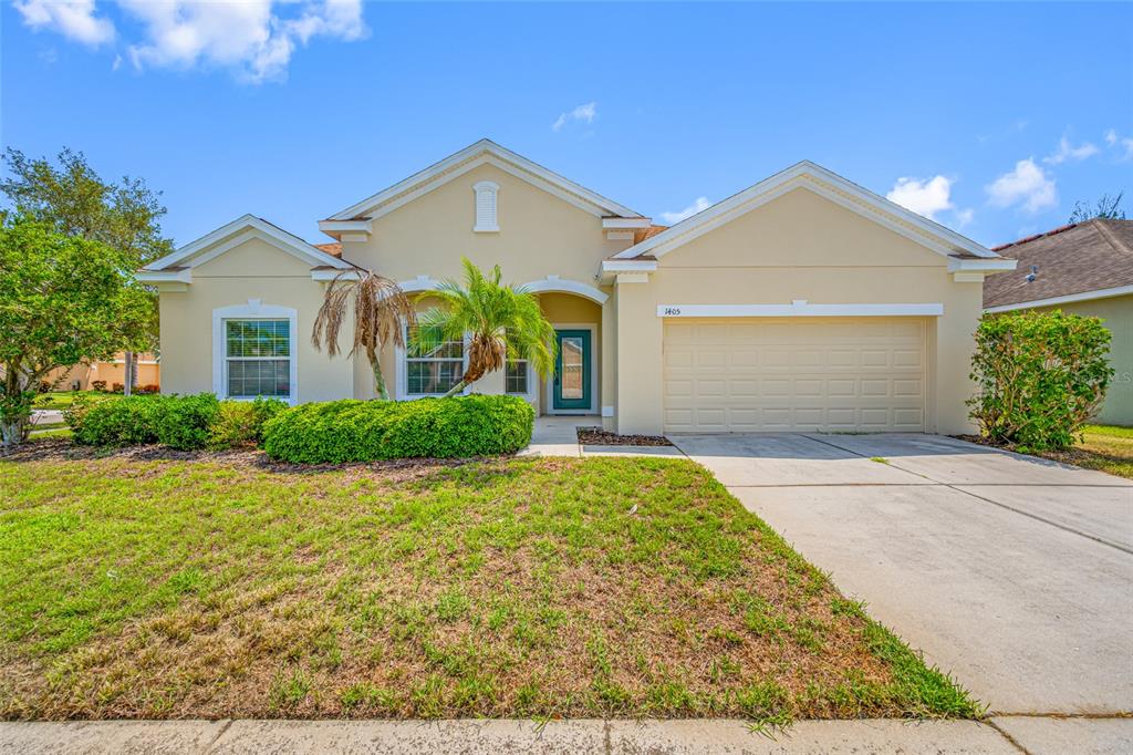 A single-story house with a beige stucco exterior, a two-car garage, and a front lawn — 1405 PARKER DEN DRIVE, RUSKIN, FL