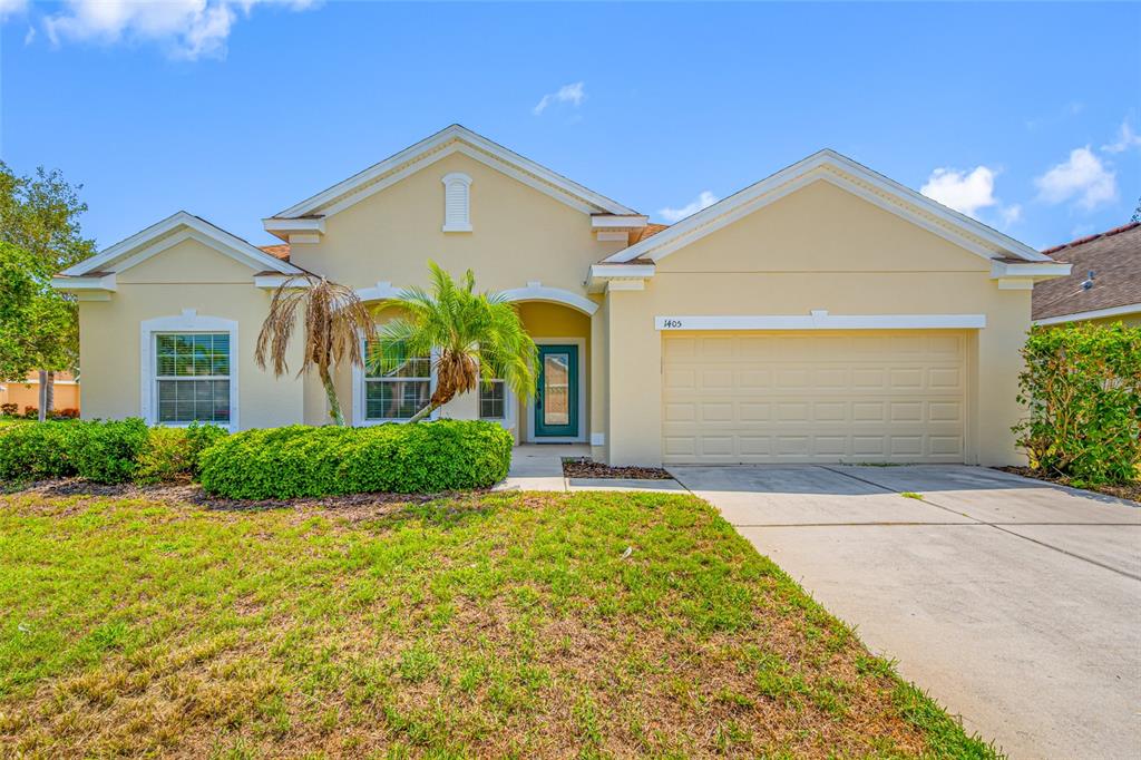 A single-story house with a beige stucco exterior, a two-car garage, and a front lawn — 1405 PARKER DEN DRIVE, RUSKIN, FL