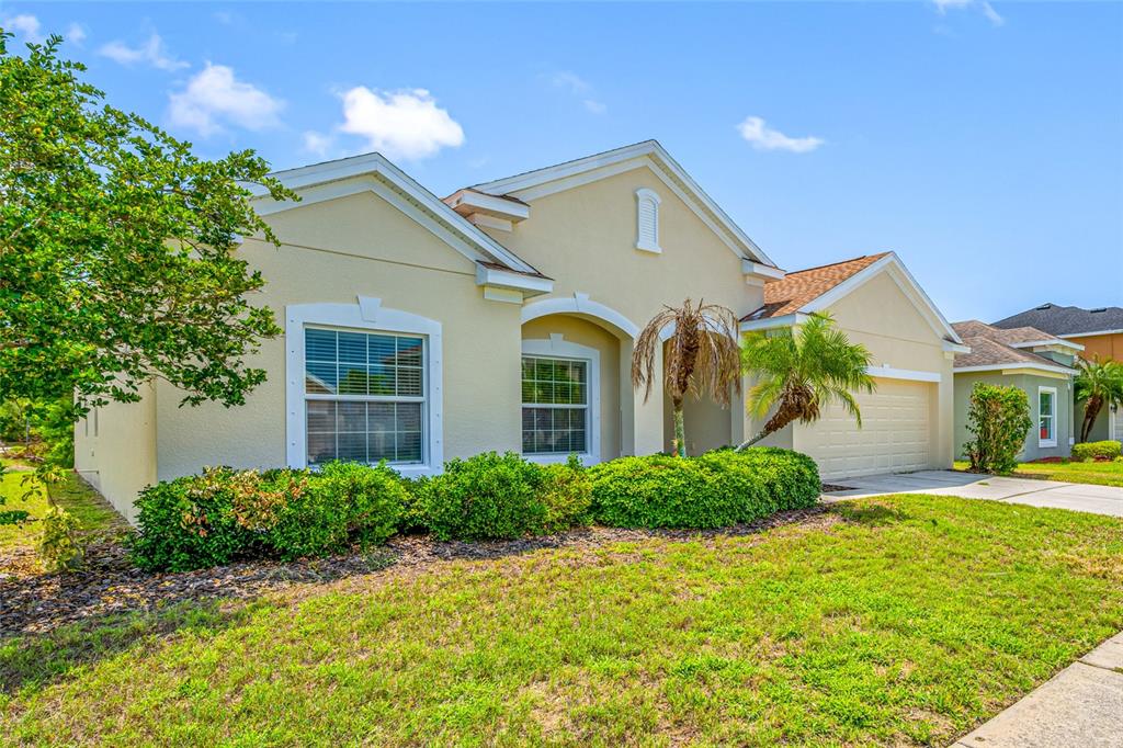 A single-story house with a beige stucco exterior, a two-car garage, and a front lawn — 1405 PARKER DEN DRIVE, RUSKIN, FL