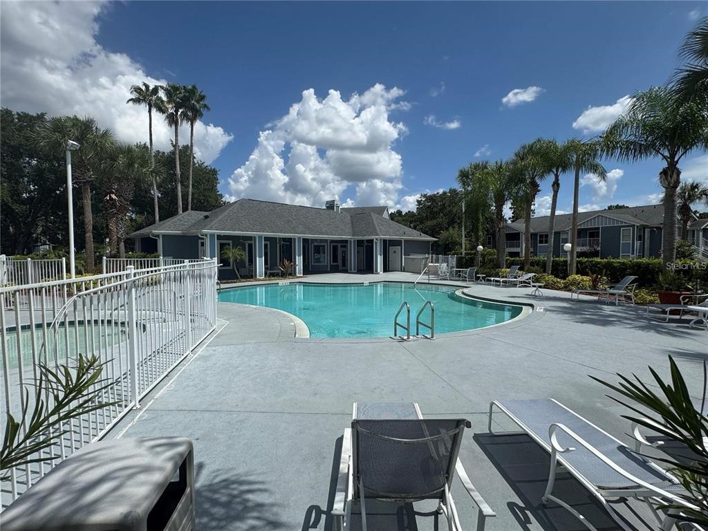 A swimming pool with lounge chairs and a clubhouse under a blue sky — 2504 GRASSY POINT DRIVE UNIT 202, LAKE MARY, FL