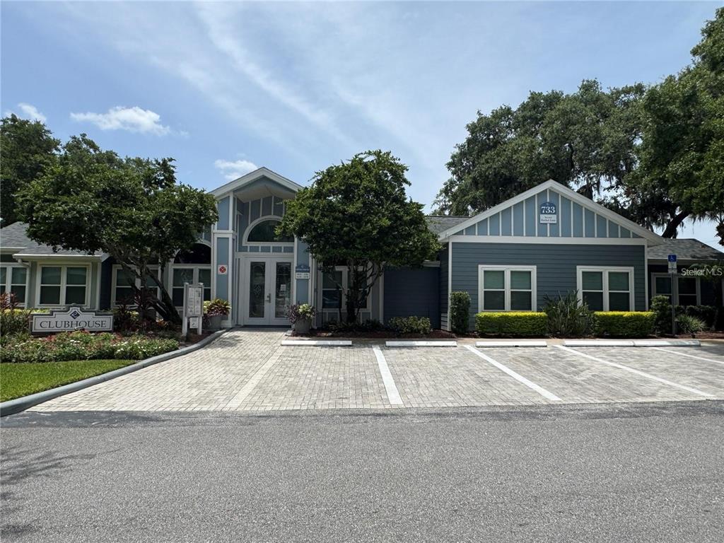 A blue clubhouse building with a paved parking area in front under a sunny sky — 2504 GRASSY POINT DRIVE UNIT 202, LAKE MARY, FL
