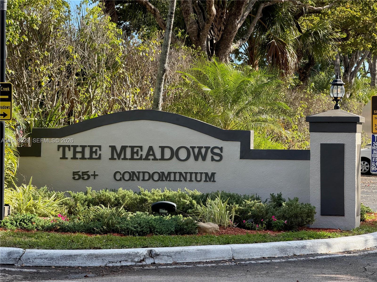 A sign for The Meadows 55+ Condominium stands in front of lush landscaping and trees — 5620 SW 3rd Pl # 114, Margate FL 33068, MARGATE, FL
