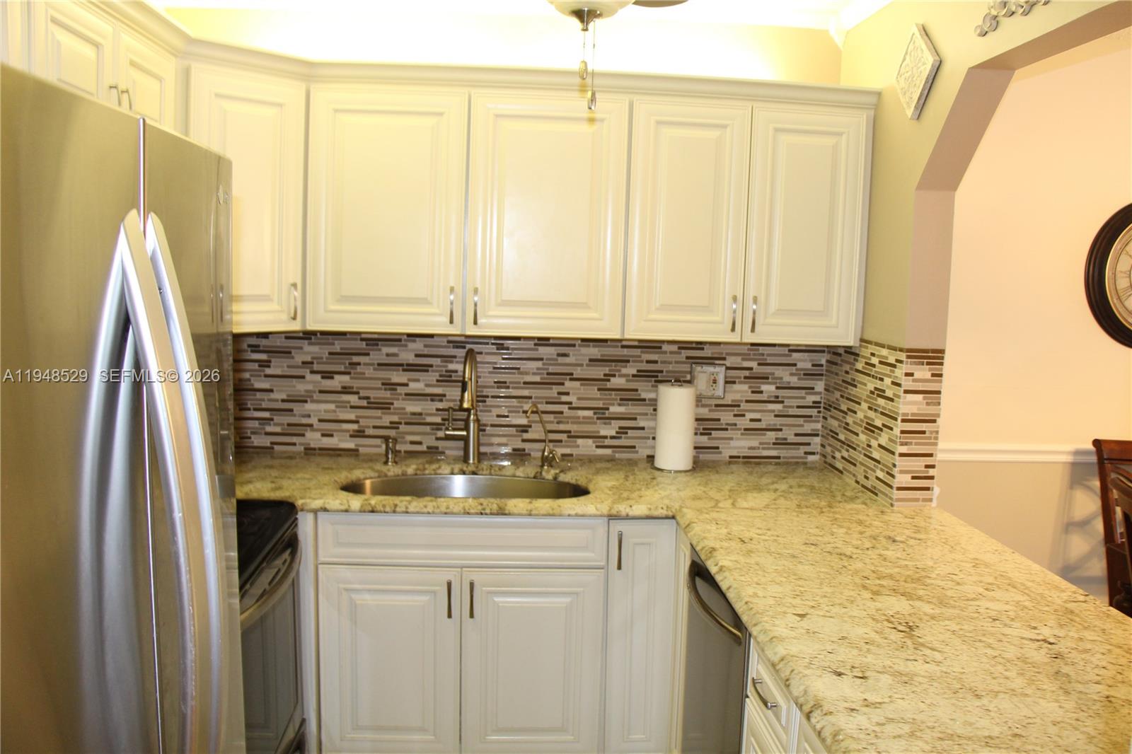 A kitchen features white cabinets, granite countertops, a stainless steel sink, and a tiled backsplash — 5620 SW 3rd Pl # 114, Margate FL 33068, MARGATE, FL