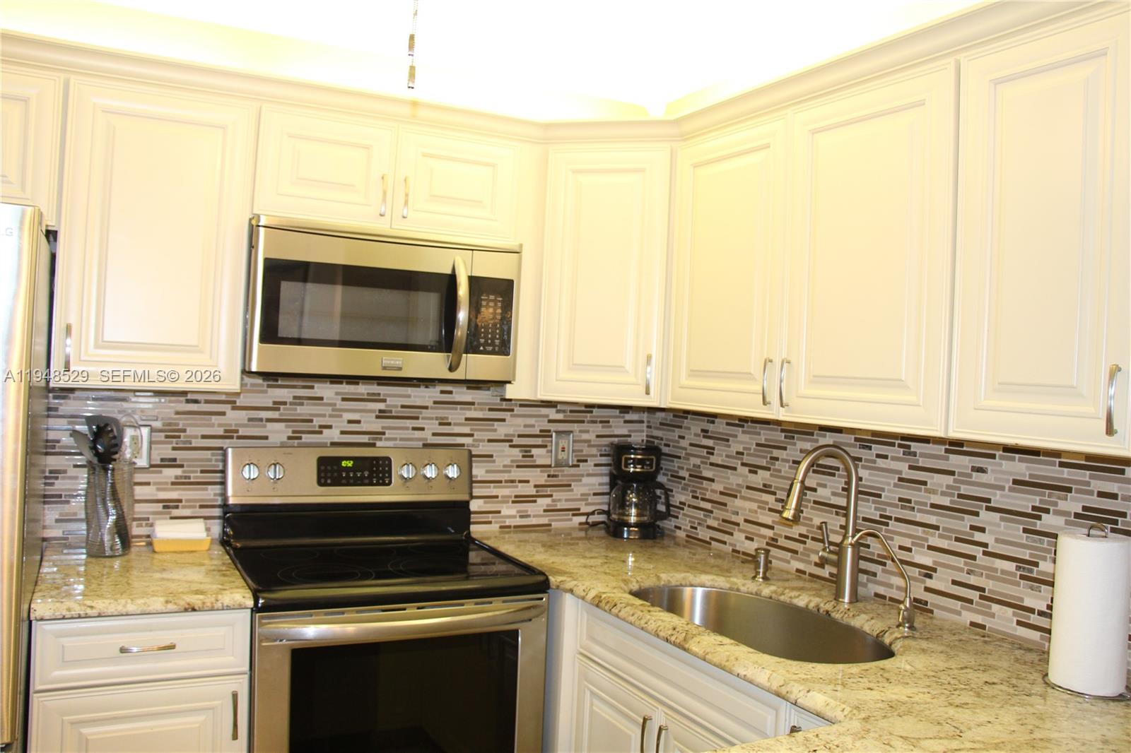 A kitchen features white cabinets, granite countertops, stainless steel appliances, and a mosaic tile backsplash — 5620 SW 3rd Pl # 114, Margate FL 33068, MARGATE, FL