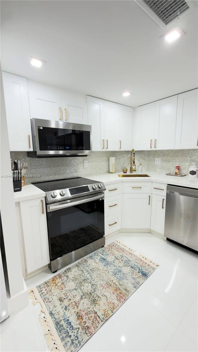 A modern kitchen features white cabinetry, stainless steel appliances, and a patterned area rug — 2333 Brickell Ave # 614, Miami FL 33129, MIAMI, FL