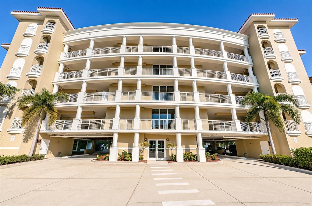 An aerial view shows a multi-story waterfront apartment building with a pool and boat docks — 3805 GULF BOULEVARD UNIT 205, ST PETE BEACH, FL