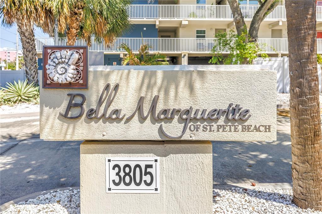 A multi-story apartment building with white balconies and columns stands above a ground-level parking area — 3805 GULF BOULEVARD UNIT 205, ST PETE BEACH, FL