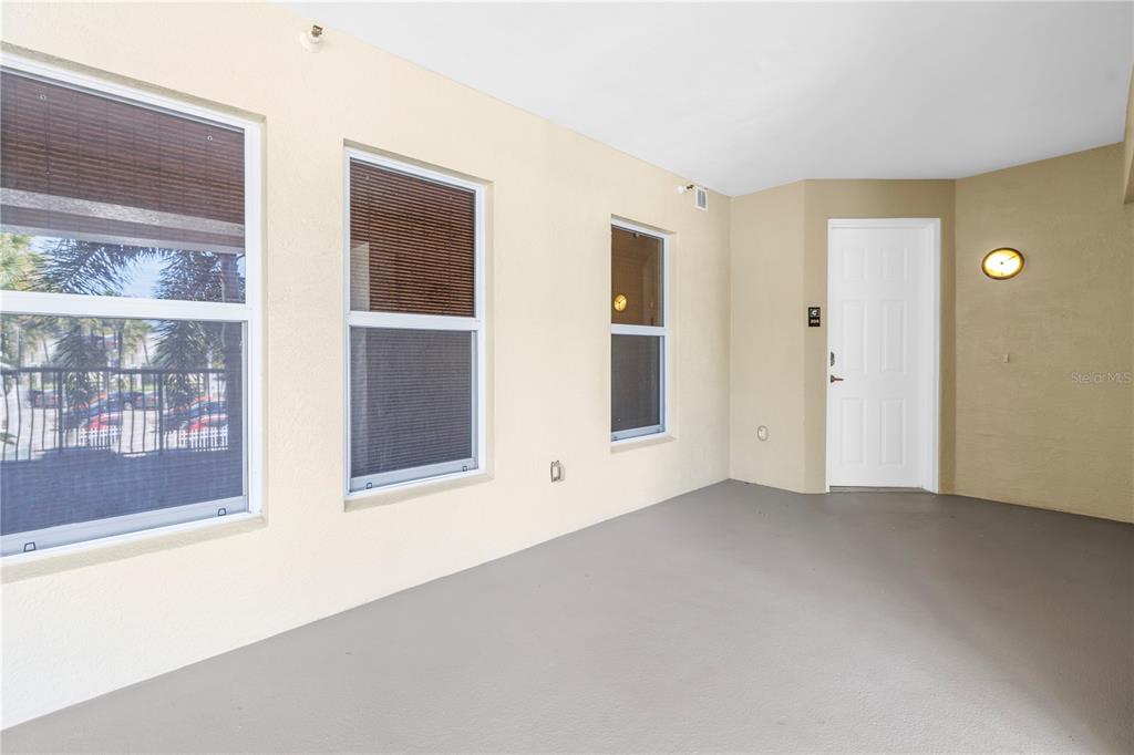 A covered patio with light-colored walls, gray flooring, three windows, and a white door — 3805 GULF BOULEVARD UNIT 205, ST PETE BEACH, FL