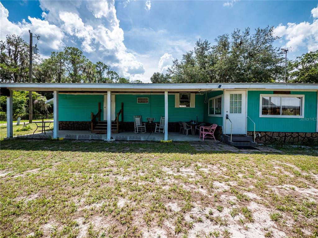 A teal mobile home features a long covered porch with outdoor furniture and stone skirting — 23673 NE 134TH LANE ROAD, FORT MC COY, FL