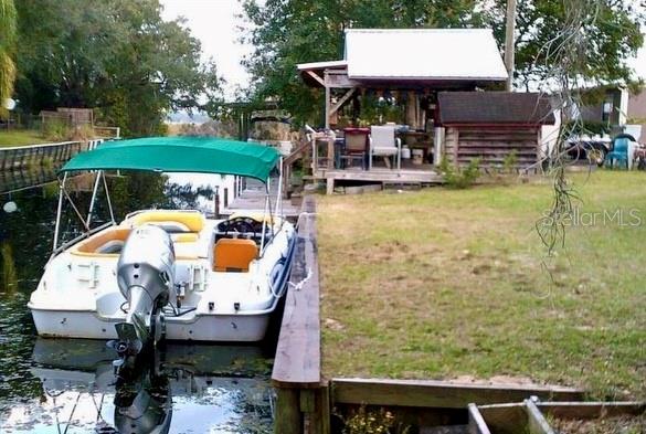A boat with a green canopy is docked next to a grassy yard and covered patio — 23673 NE 134TH LANE ROAD, FORT MC COY, FL