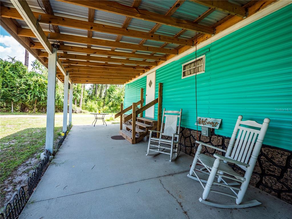 A covered concrete porch features two white rocking chairs and wooden stairs leading to a door — 23673 NE 134TH LANE ROAD, FORT MC COY, FL