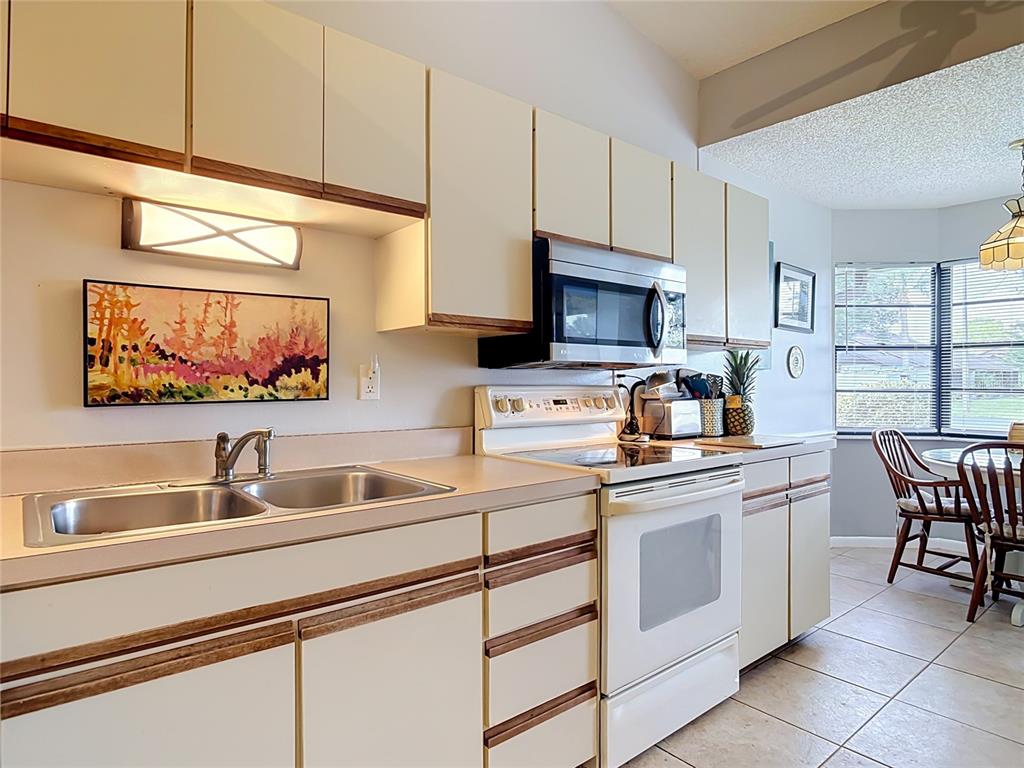 A kitchen features off-white cabinets with wood trim, a double sink, and white appliances — 935 EASTRIDGE DRIVE UNIT 7A, DEBARY, FL