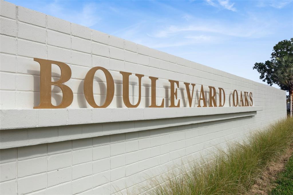 A white brick wall displays the gold metal lettering for Boulevard Oaks under a blue sky — 446 SKYFIELD COURT, LADY LAKE, FL