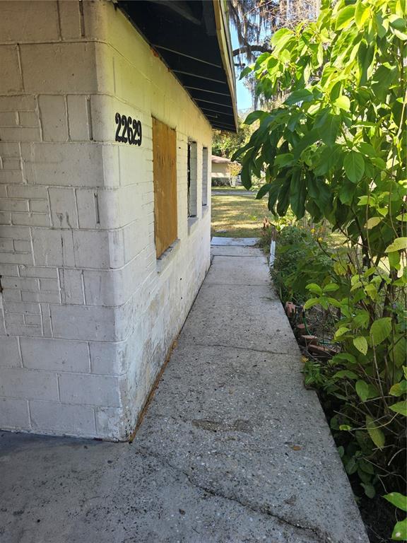 A concrete walkway runs alongside a white painted block building with boarded-up windows — 22629 SE 71ST AVENUE, HAWTHORNE, FL