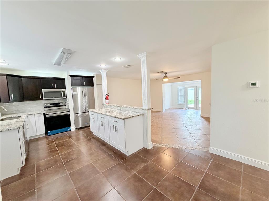 A kitchen with white and dark cabinets, granite countertops, and tile flooring opens to a living area — 1827 OKLAHOMA AVENUE NE, ST PETERSBURG, FL