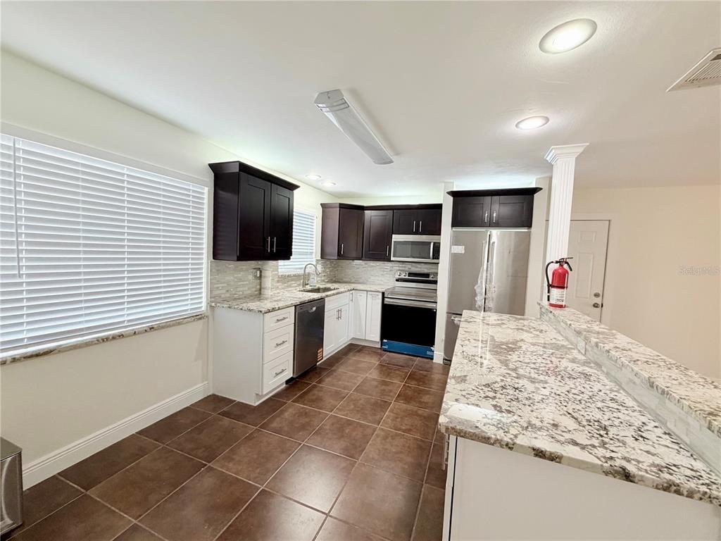 A kitchen features dark upper cabinets, white lower cabinets, granite countertops, and brown tile flooring — 1827 OKLAHOMA AVENUE NE, ST PETERSBURG, FL