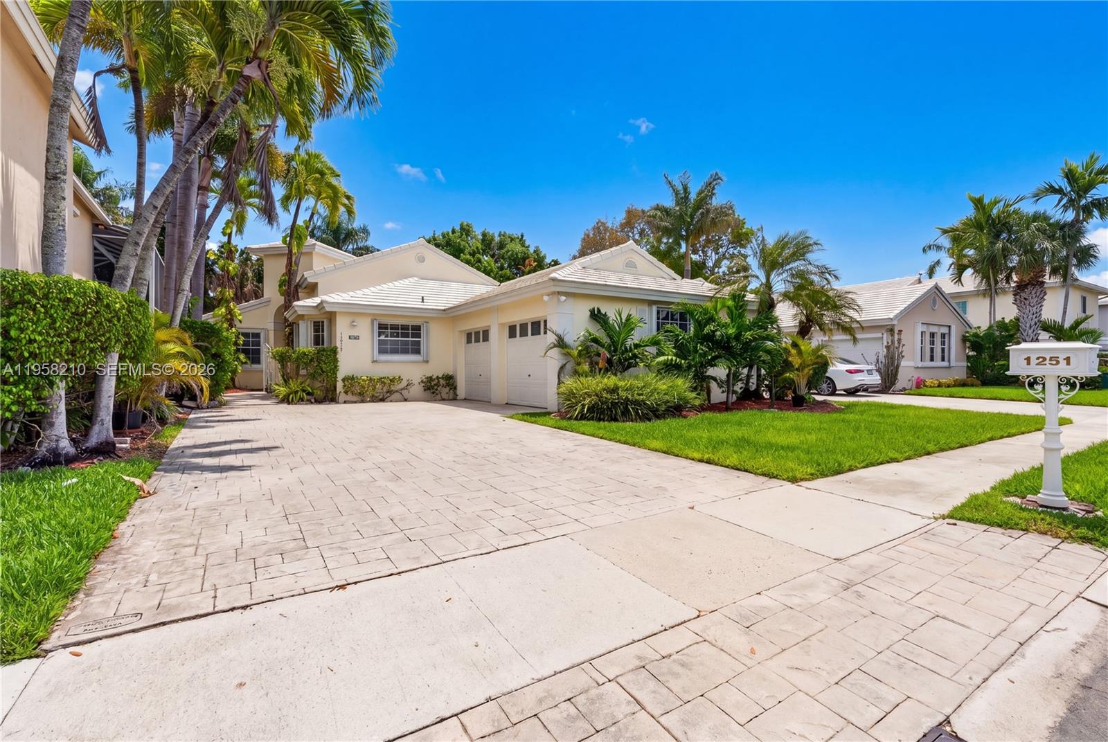 A single-story house with a paved driveway, two-car garage, and palm trees under a blue sky — 1251 E Wilshire Cir E, Pembroke Pines FL 33027, PEMBROKE PINES, FL