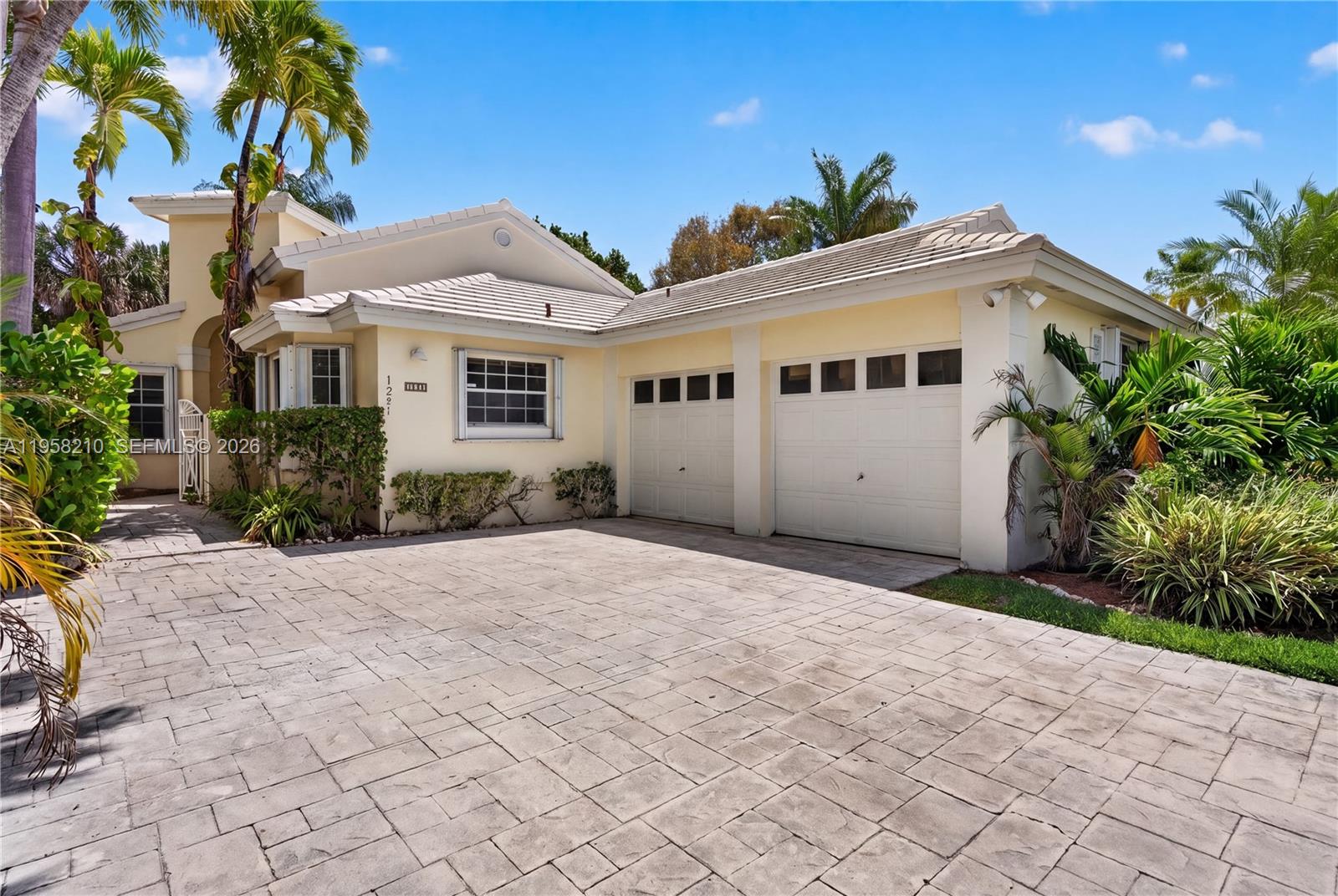 A light yellow house with a two-car garage and a paved driveway under a blue sky — 1251 E Wilshire Cir E, Pembroke Pines FL 33027, PEMBROKE PINES, FL